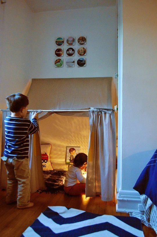 Two children playing in a blanket fort constructed with tension rods.