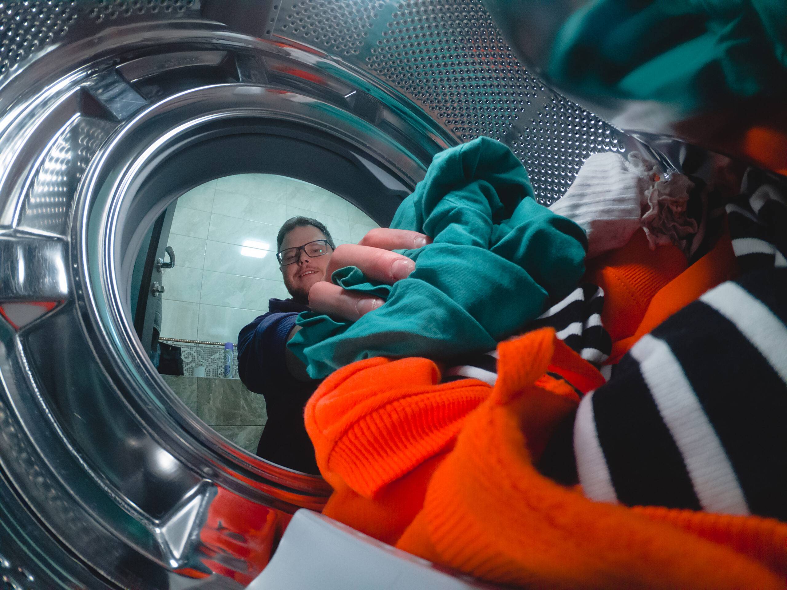 A guy puts dirty clothes in the washing machine