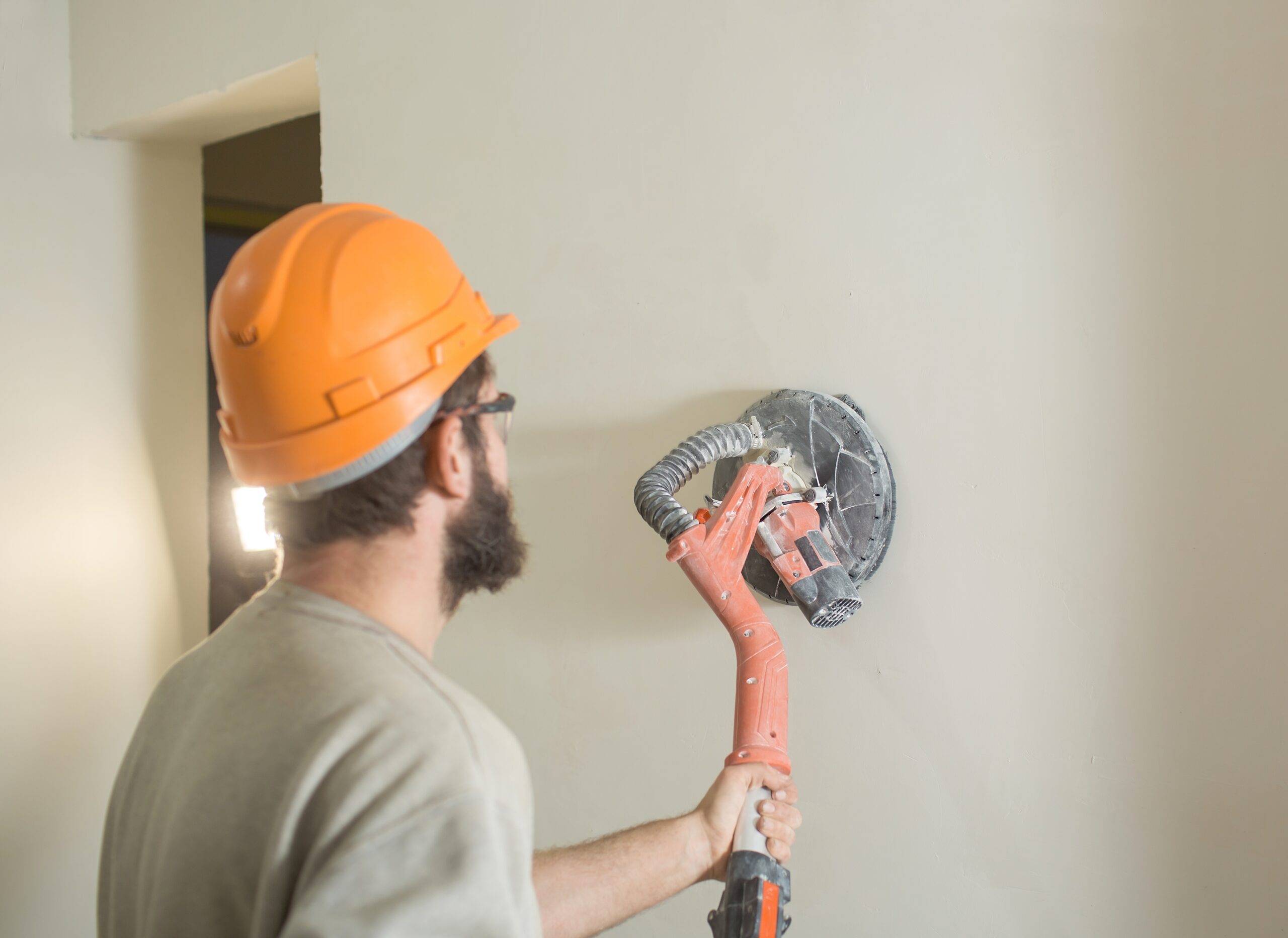 a man with a beard in a construction helmet skins the walls with an electric grinder