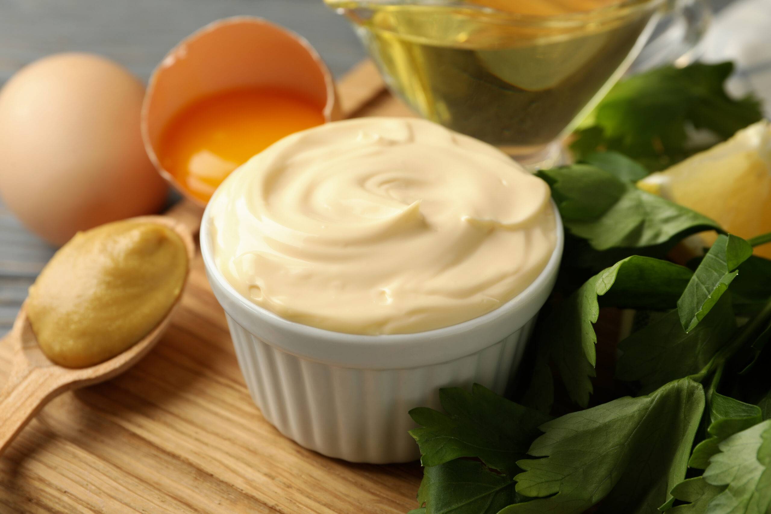 Board with bowl of mayonnaise and ingredients for cooking on wooden background