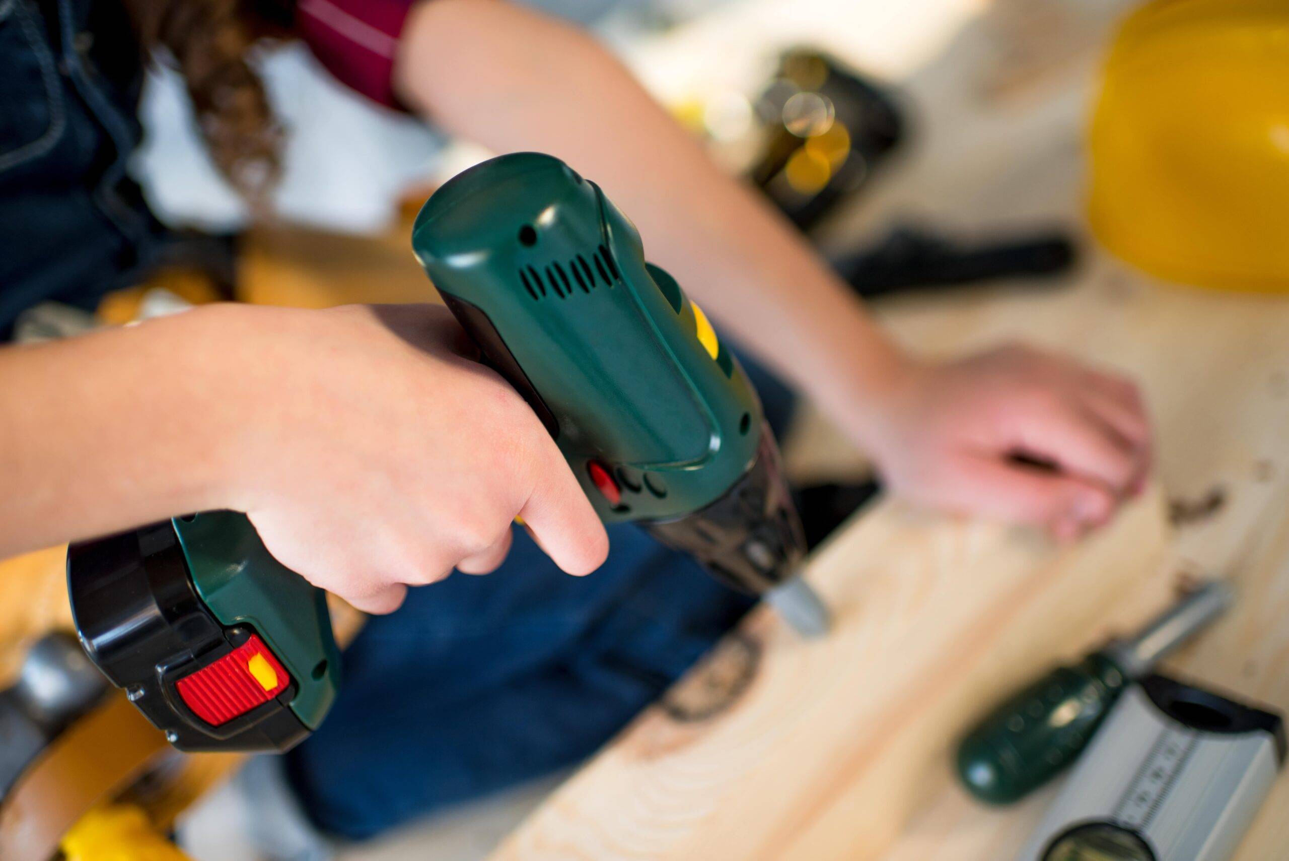 A person using a drill against a wood plank.