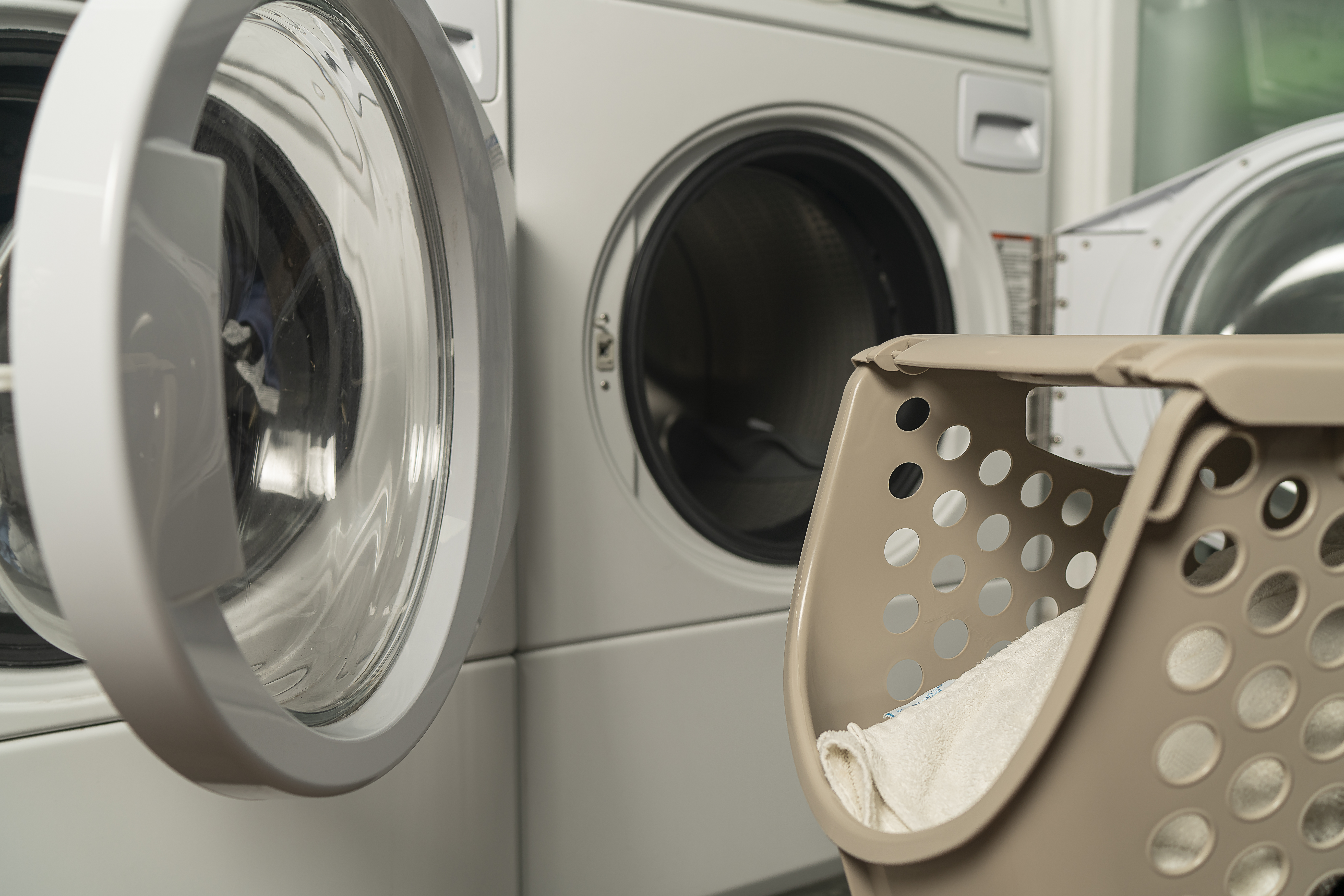 Close up view of a laundry baskets and an opened washer. Unrecognizable male standing working in laundry room.