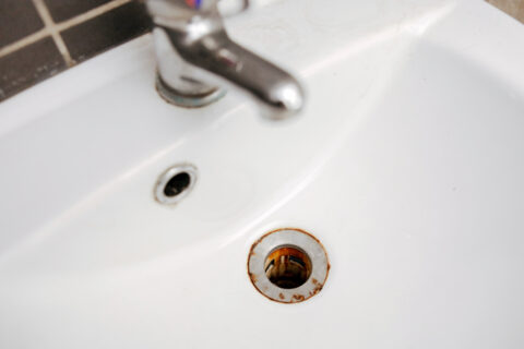 Dirty and rusty washbasin, close up view. Metal drain hole with red rust stain. Corrosion, unsanitary. Stained bathroom plumbing.