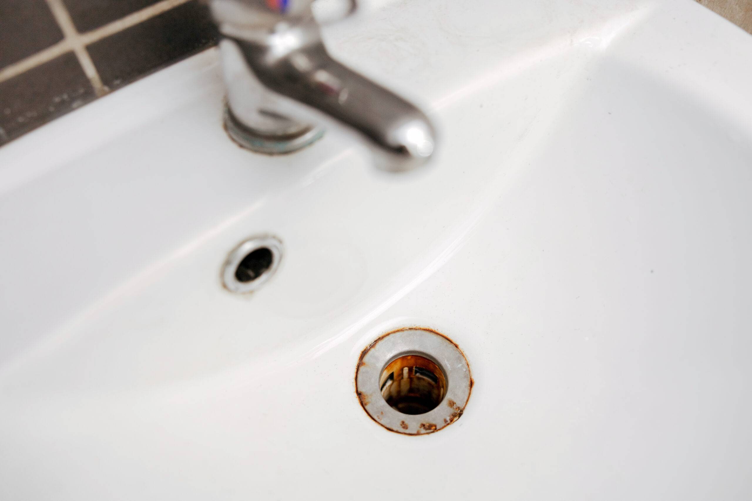 Dirty and rusty washbasin, close up view. Metal drain hole with red rust stain. Corrosion, unsanitary. Stained bathroom plumbing.