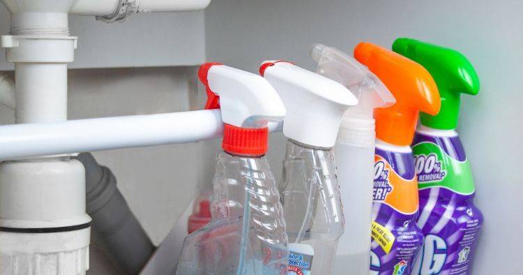 A tension rod under a sink holding spray bottles by their triggers.