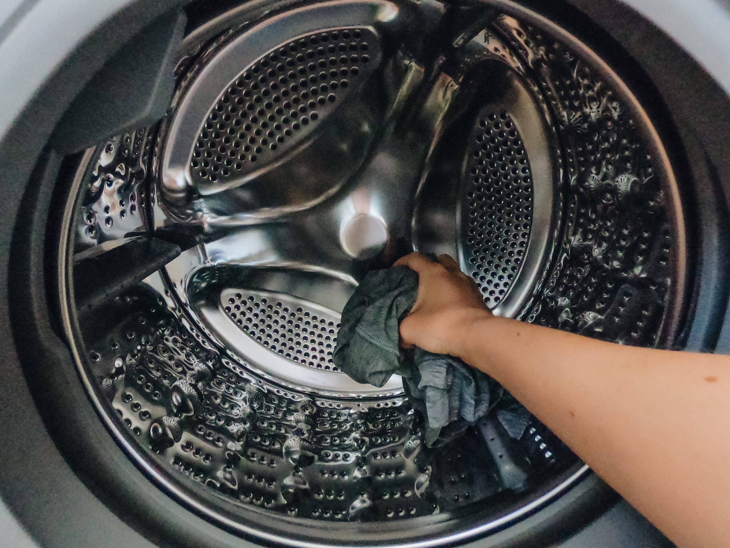 A person putting a single rag into a washing machine drum.