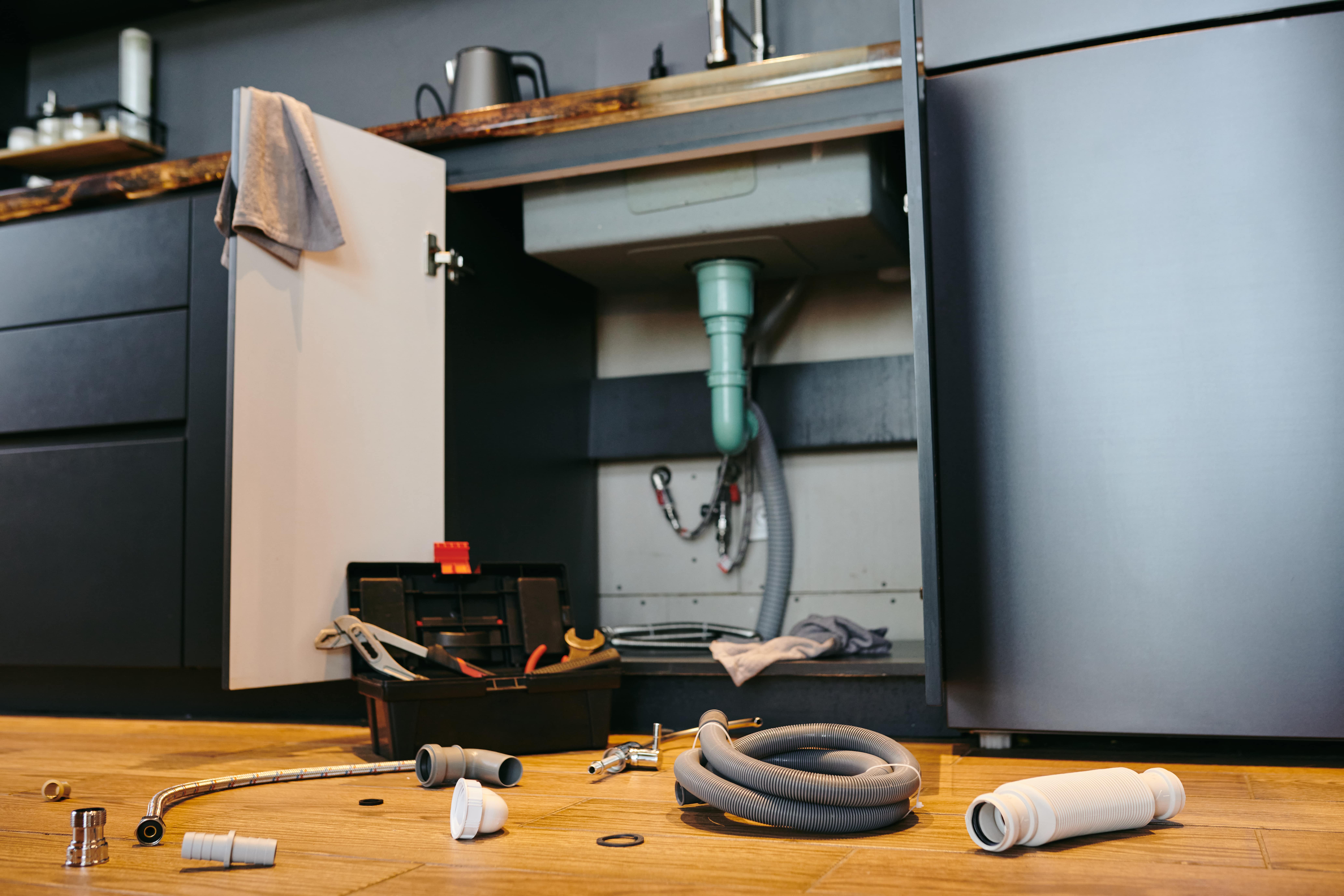 An under-the-sink cabinet that's open, plumbing tools scattered about.