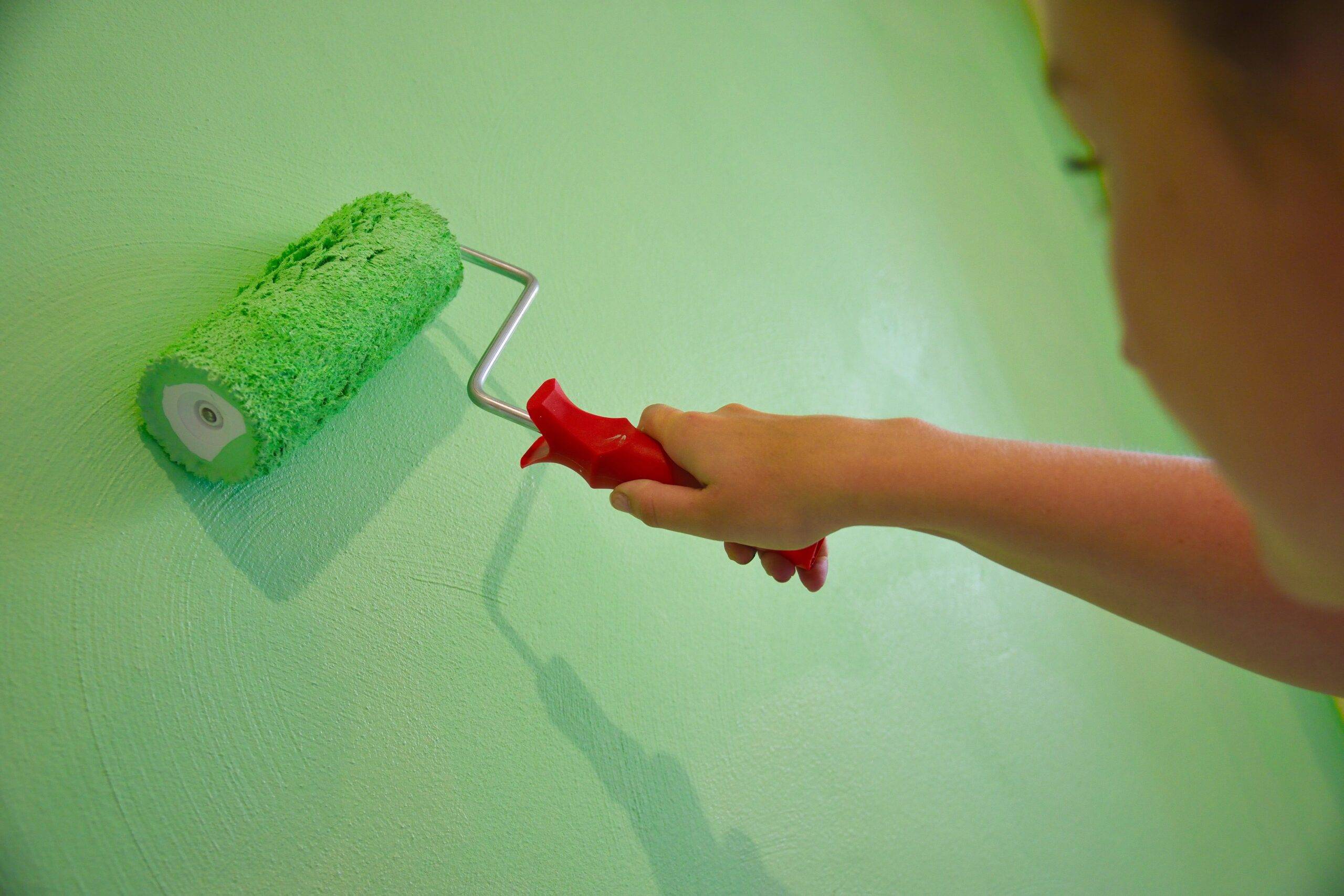A close photo of someone painting a wall green with a short-handled paint roller.
