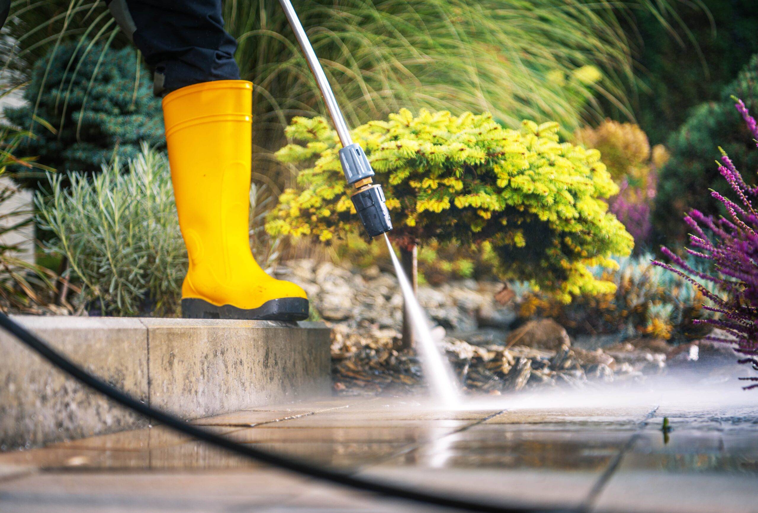 A person in yellow rubber boots pressure washing steps they're standing on.