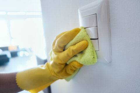 Close up view of person wiping electrical and light switches at home. People cleaning and disinfecting domestic surfaces to prevent virus and bacteria spread.