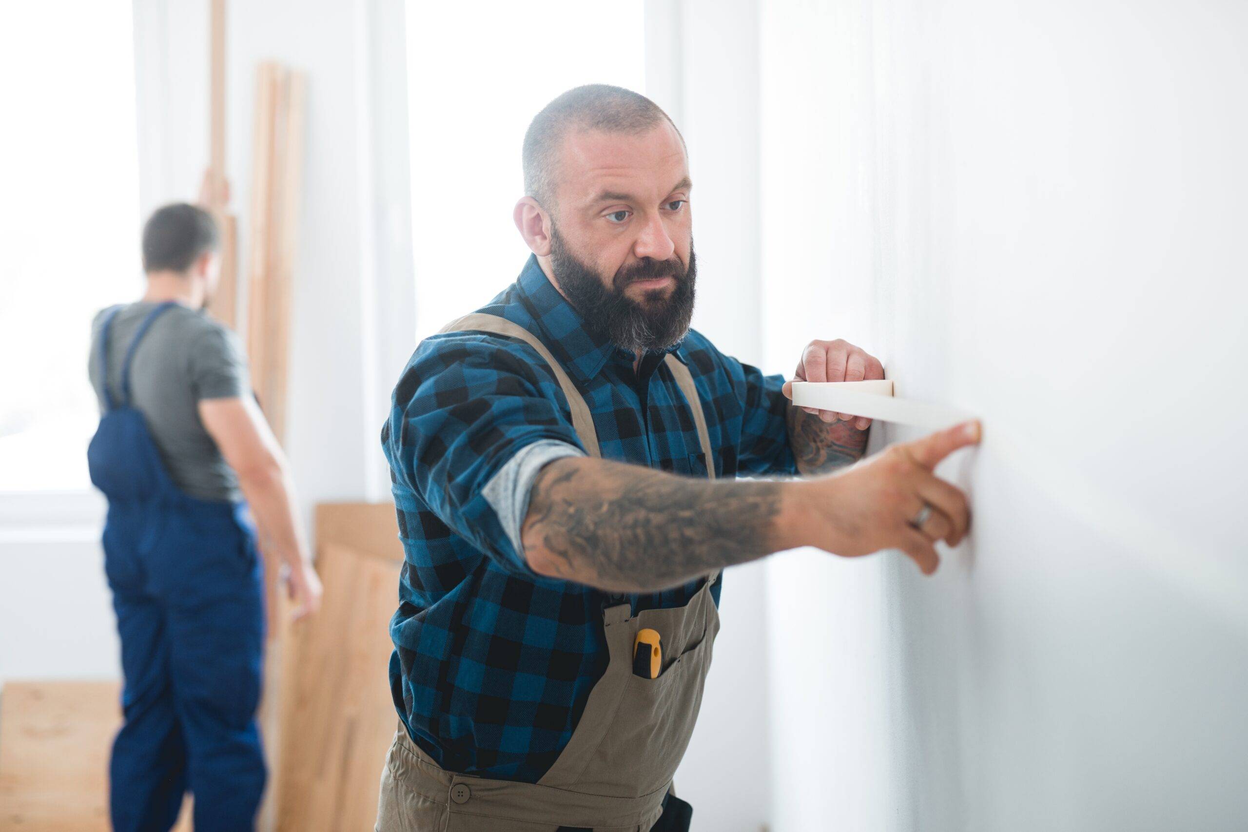 Professional builder puts a tape on an empty wall before painting it