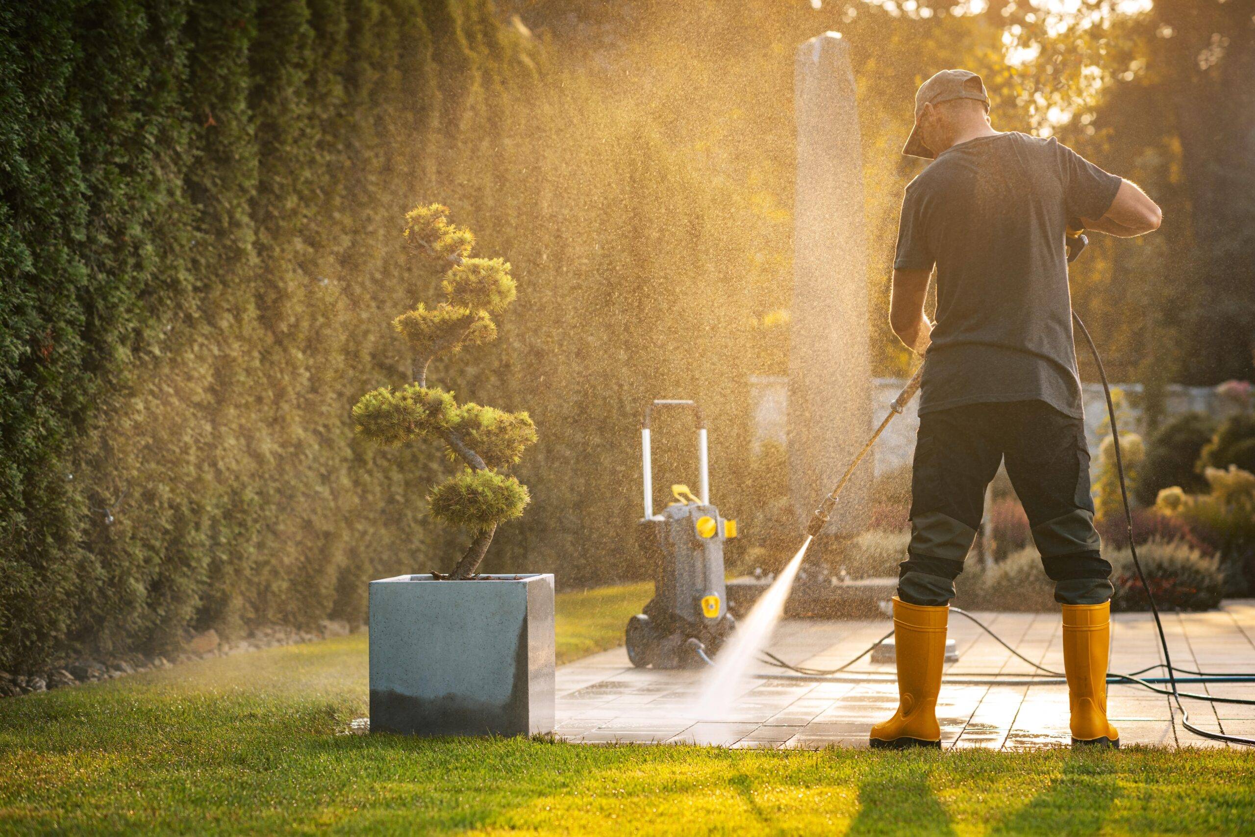 A person standing and pressure washing a back patio.