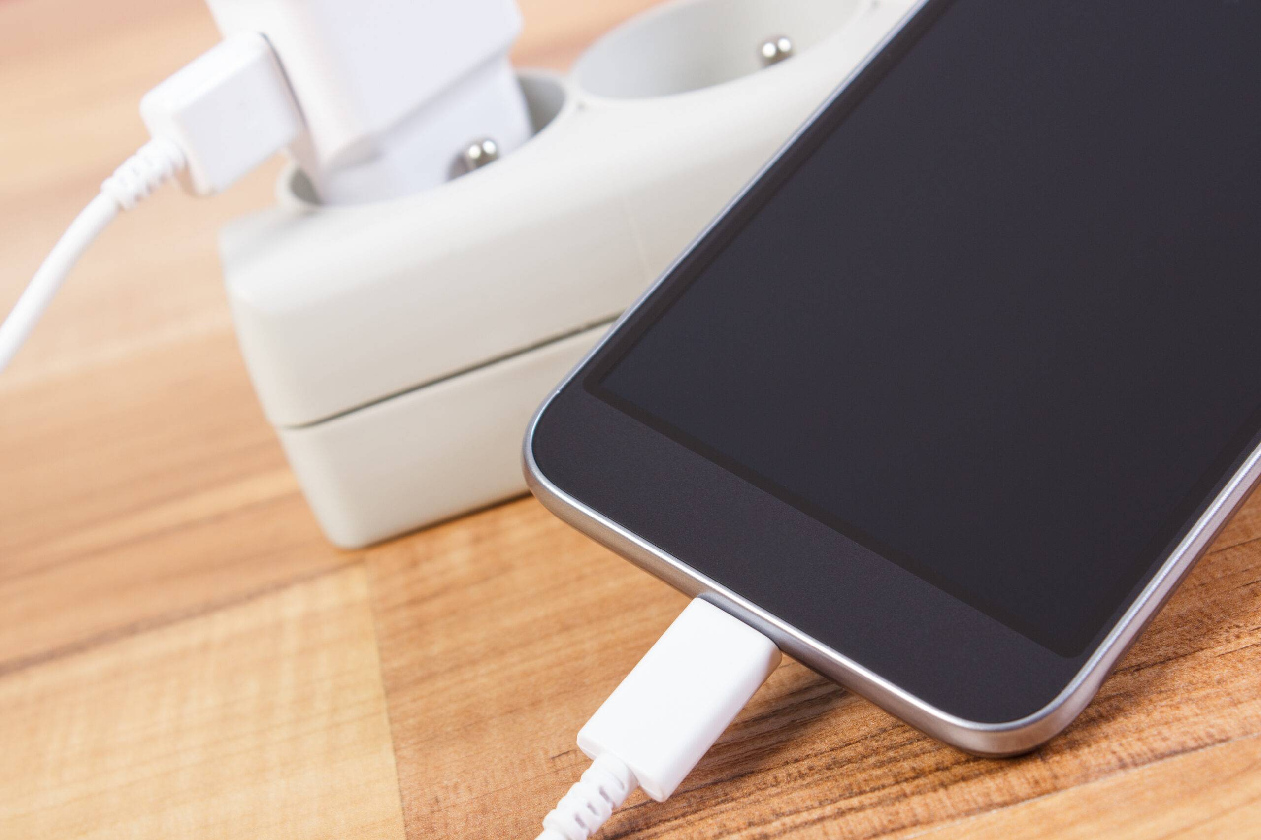 Mobile phone with connected plug of charger, smartphone charging on table
