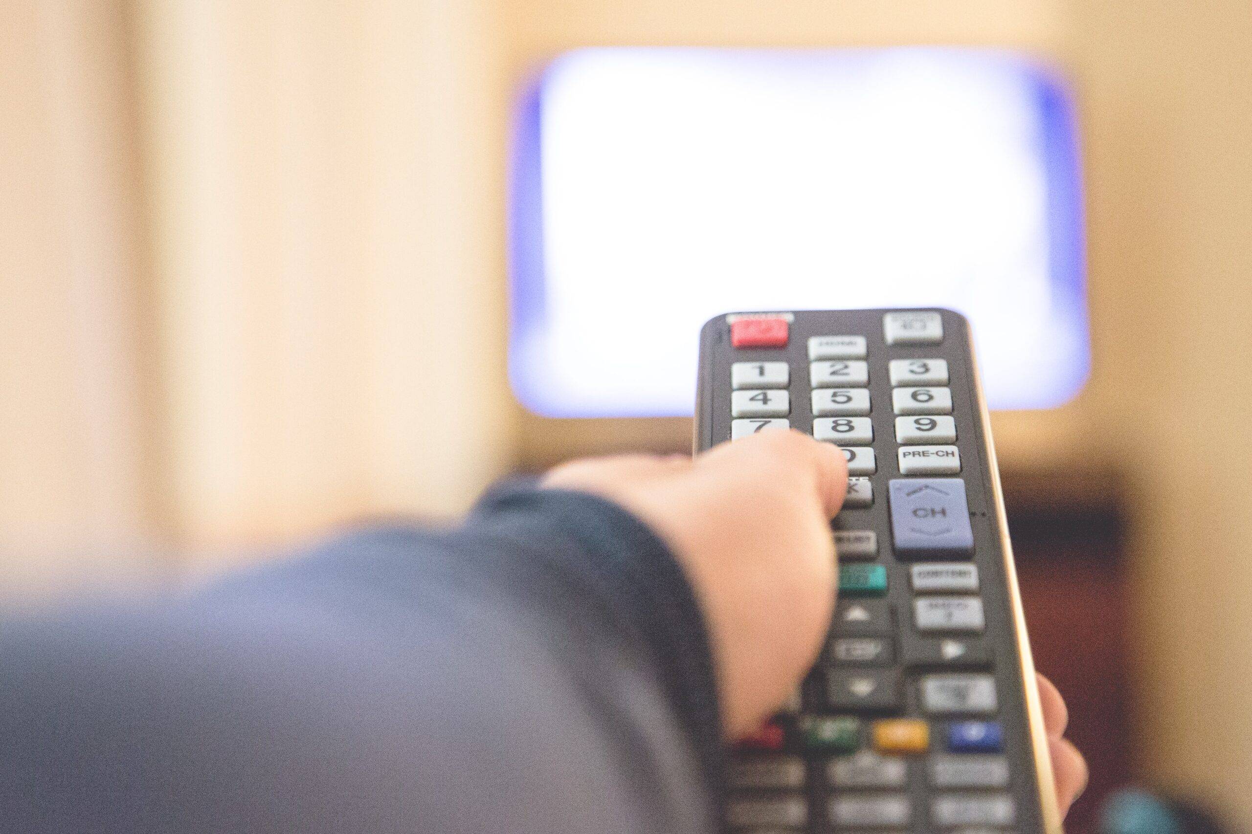 A hand holding a TV remote and pointing it forward.