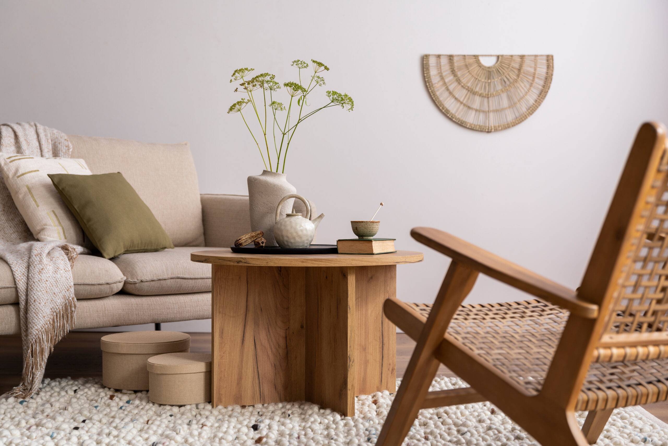Warm and cozy interior of living room with beige sofa, pillow, wooden coffee table, decoration, armchair and elegant personal accessories. Beige wall. Home decor. Template.