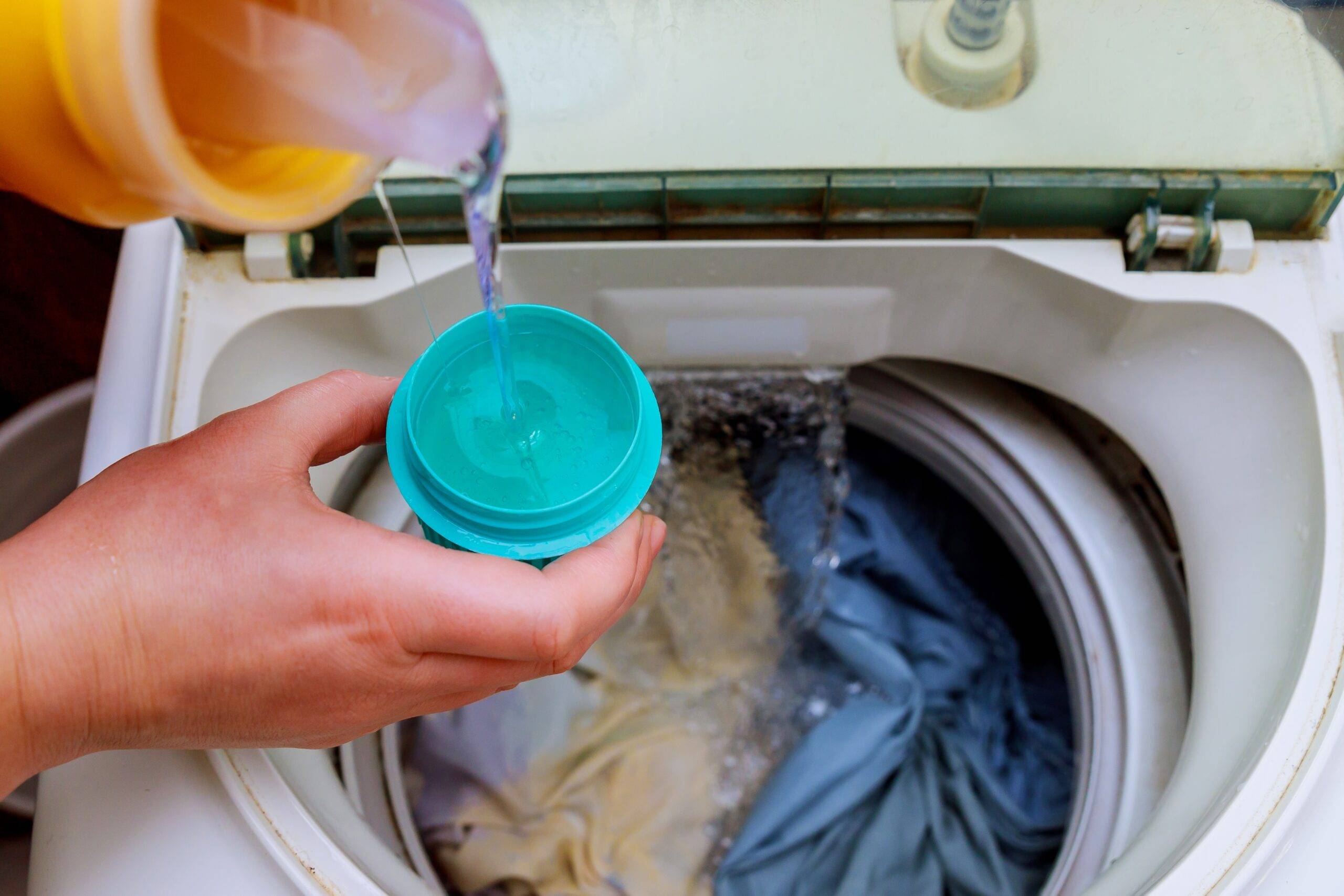Woman hand pouring laundry detergent into the washing machine