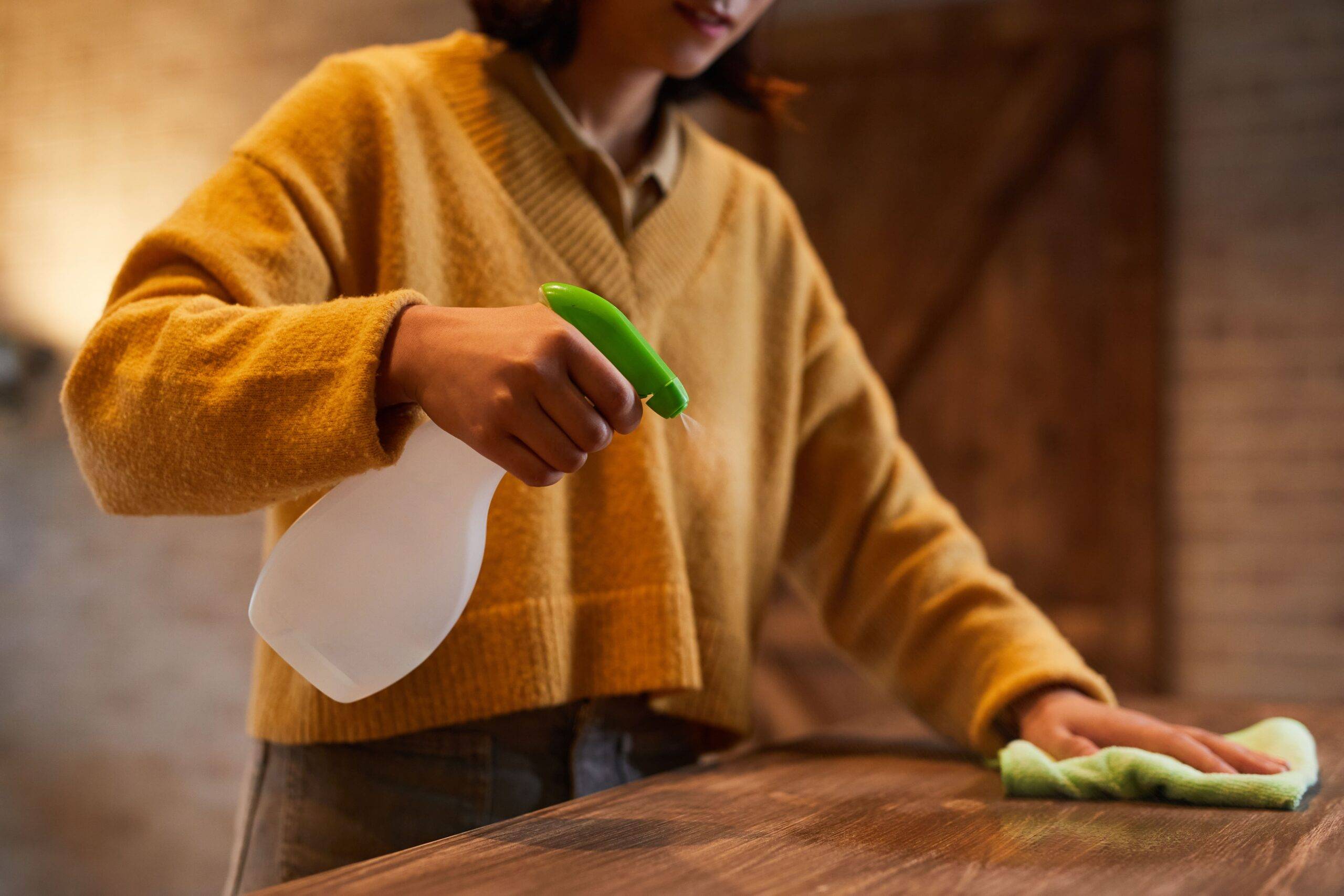 A woman spraying and cleaning a wood table.