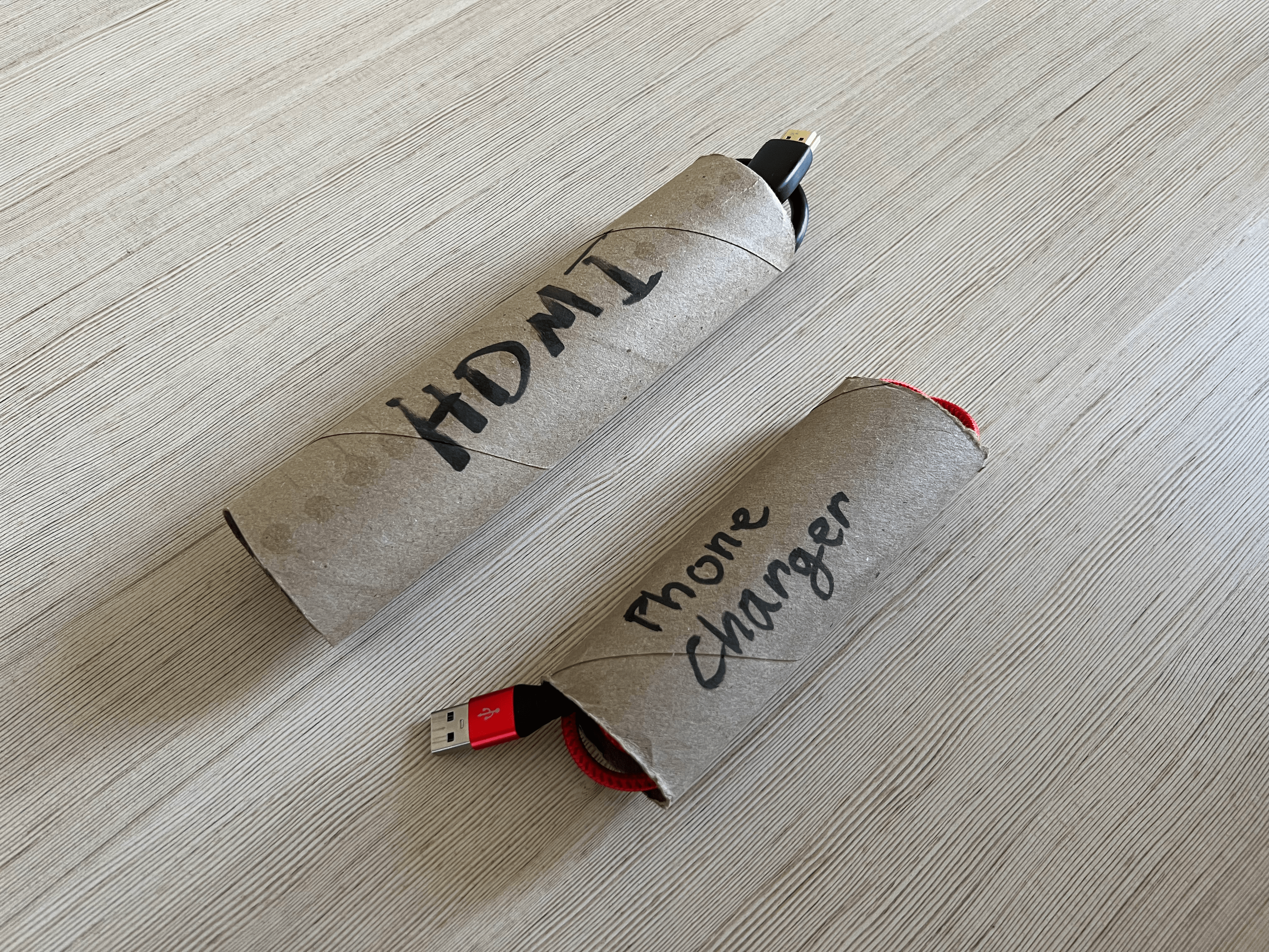Two paper towel rolls, cut to size, with wound up cables inside them, those cables labeled on the outside of the tube.