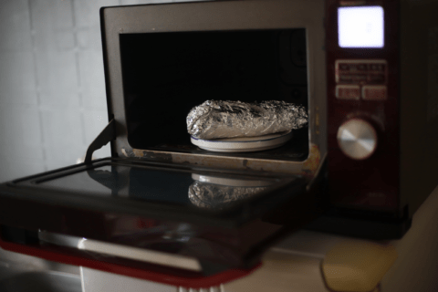 Food covered in aluminum foil in an oven with door open.