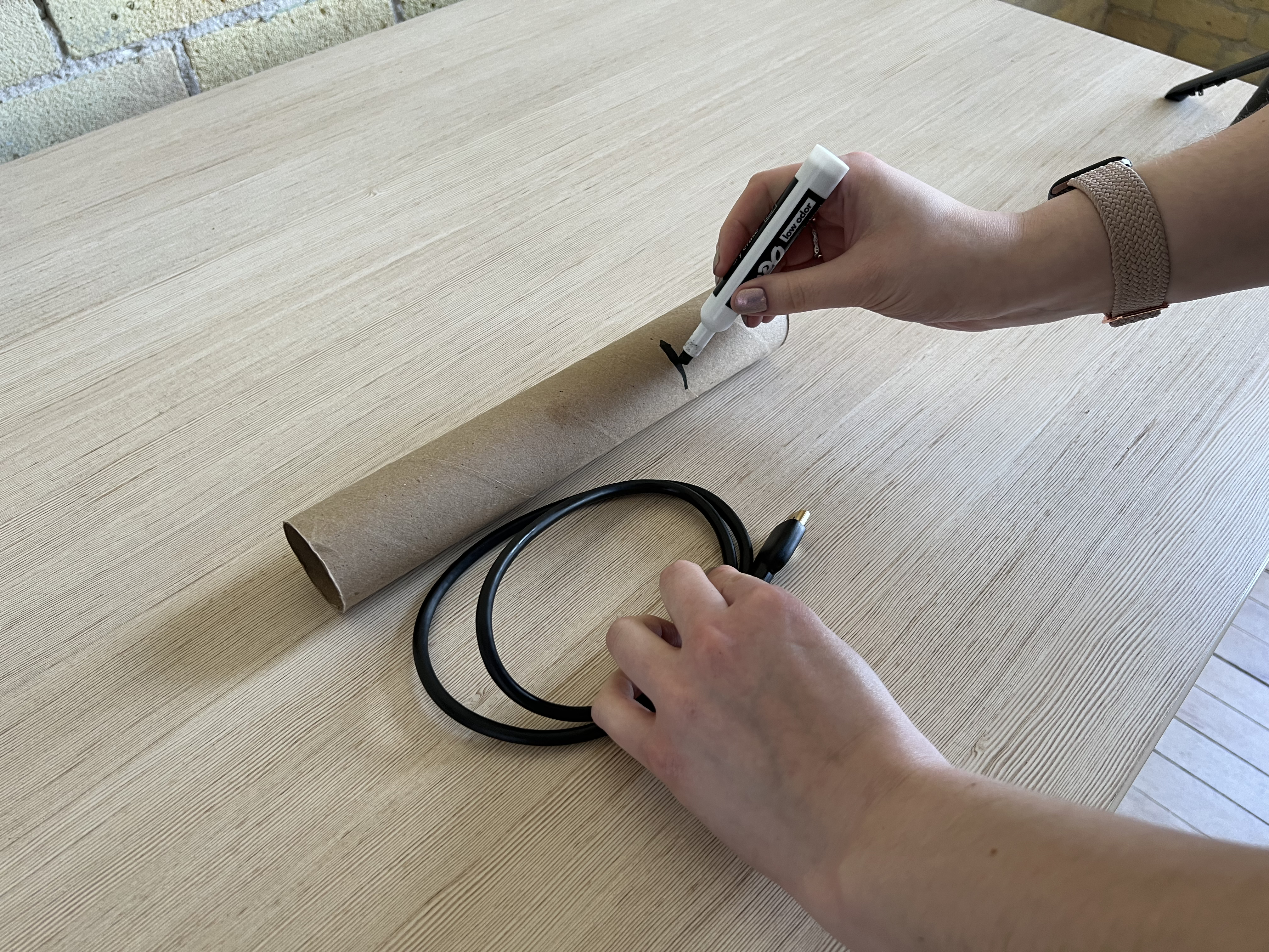 A pair of hands, one holding a rolled up cable, the other drawing a marker line to the same size on a paper towel tube.