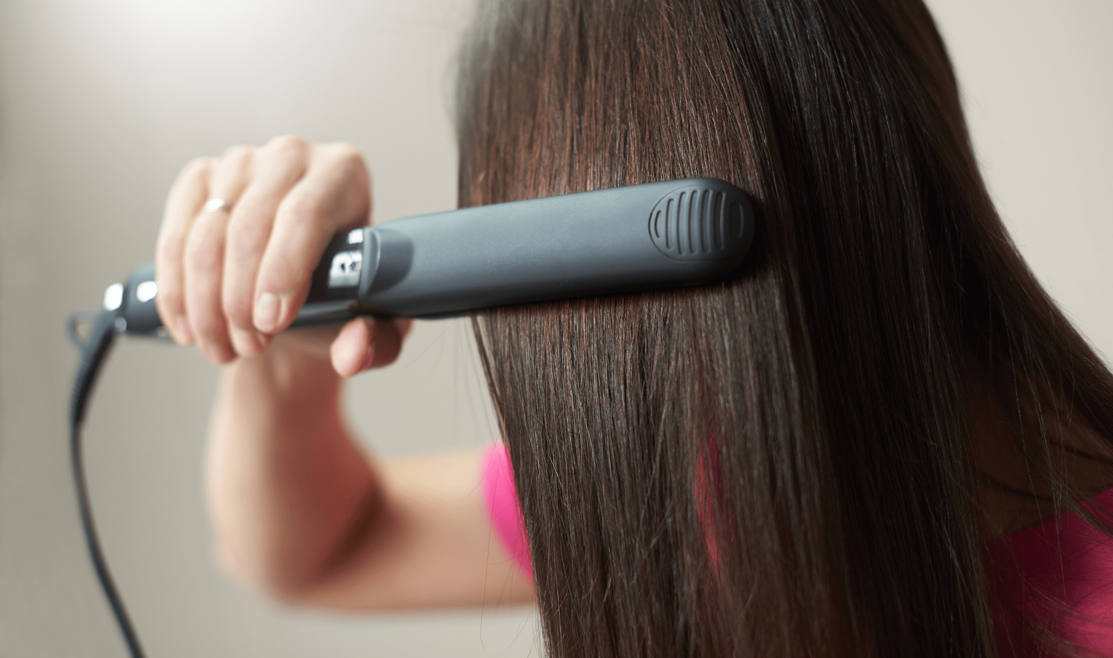 A woman using a hair straightener on her hair.