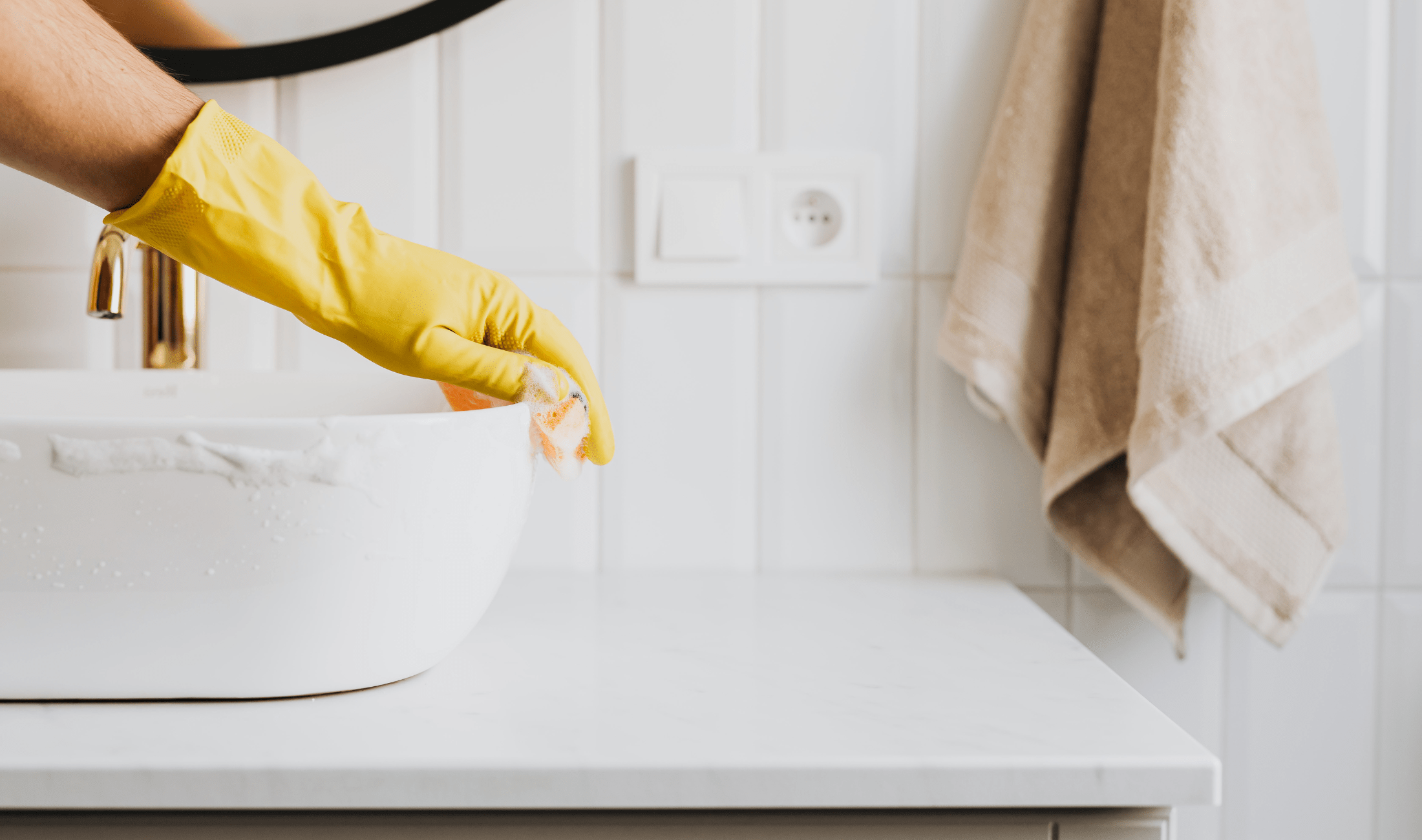 A yellow-gloved hand cleaning a bathroom sink.