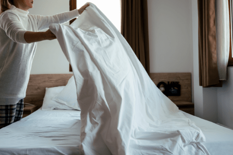 Person placing bed sheets on bed.