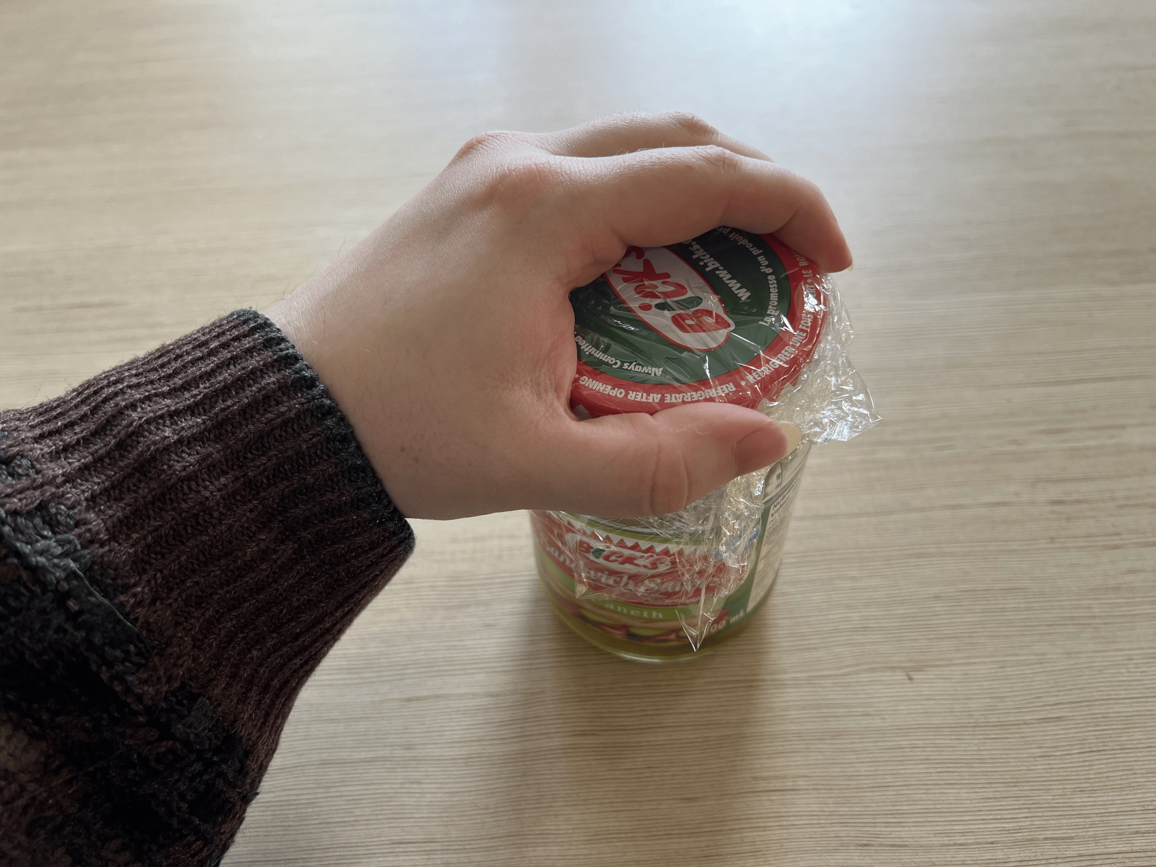 A hand over the jar lid that's now covered in plastic wrap.