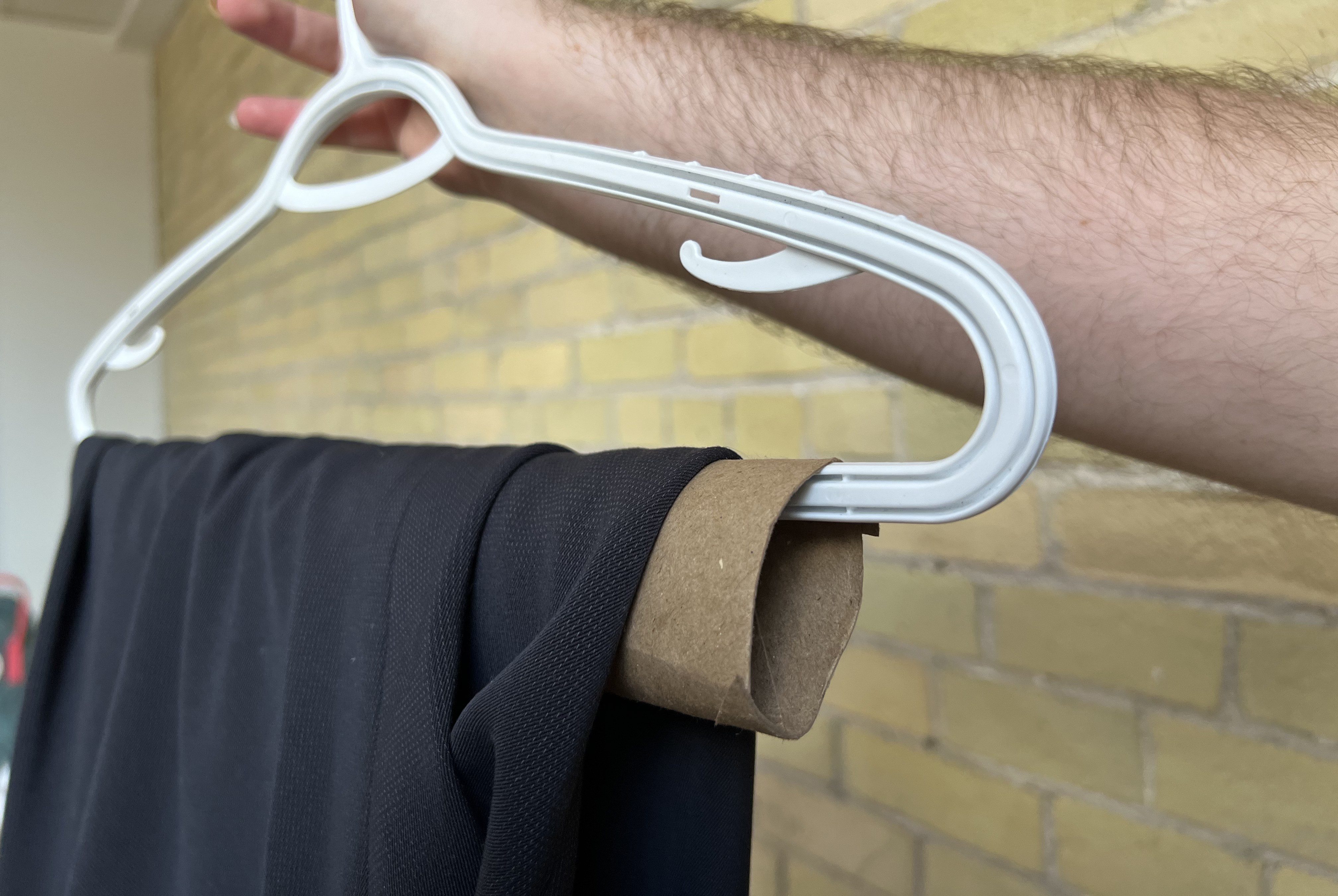 A hand holding up a plastic hanger that has the cardboard tube on it and a pair of pants folded over the tube.