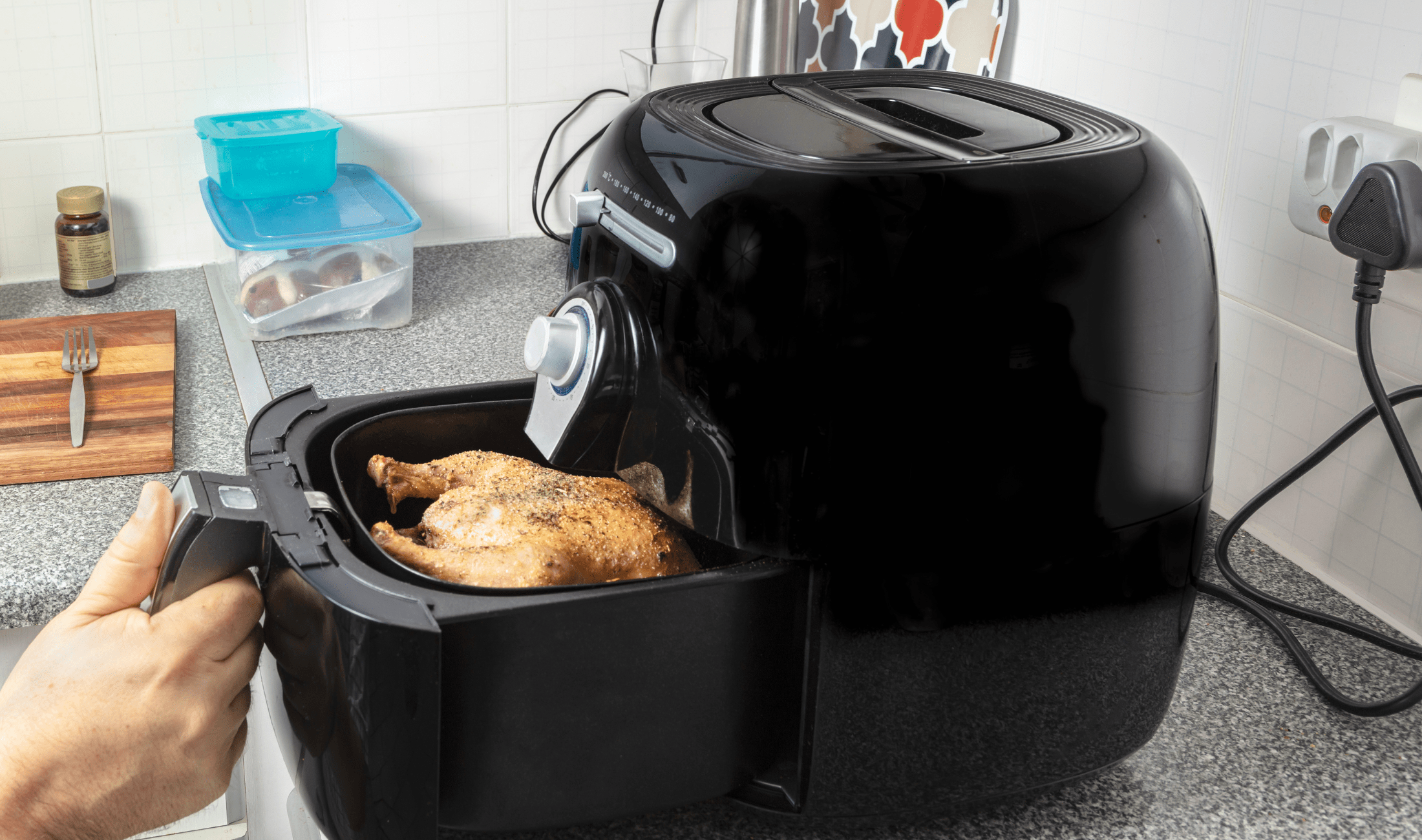 A hand opening an air fryer basket with a chicken in it.