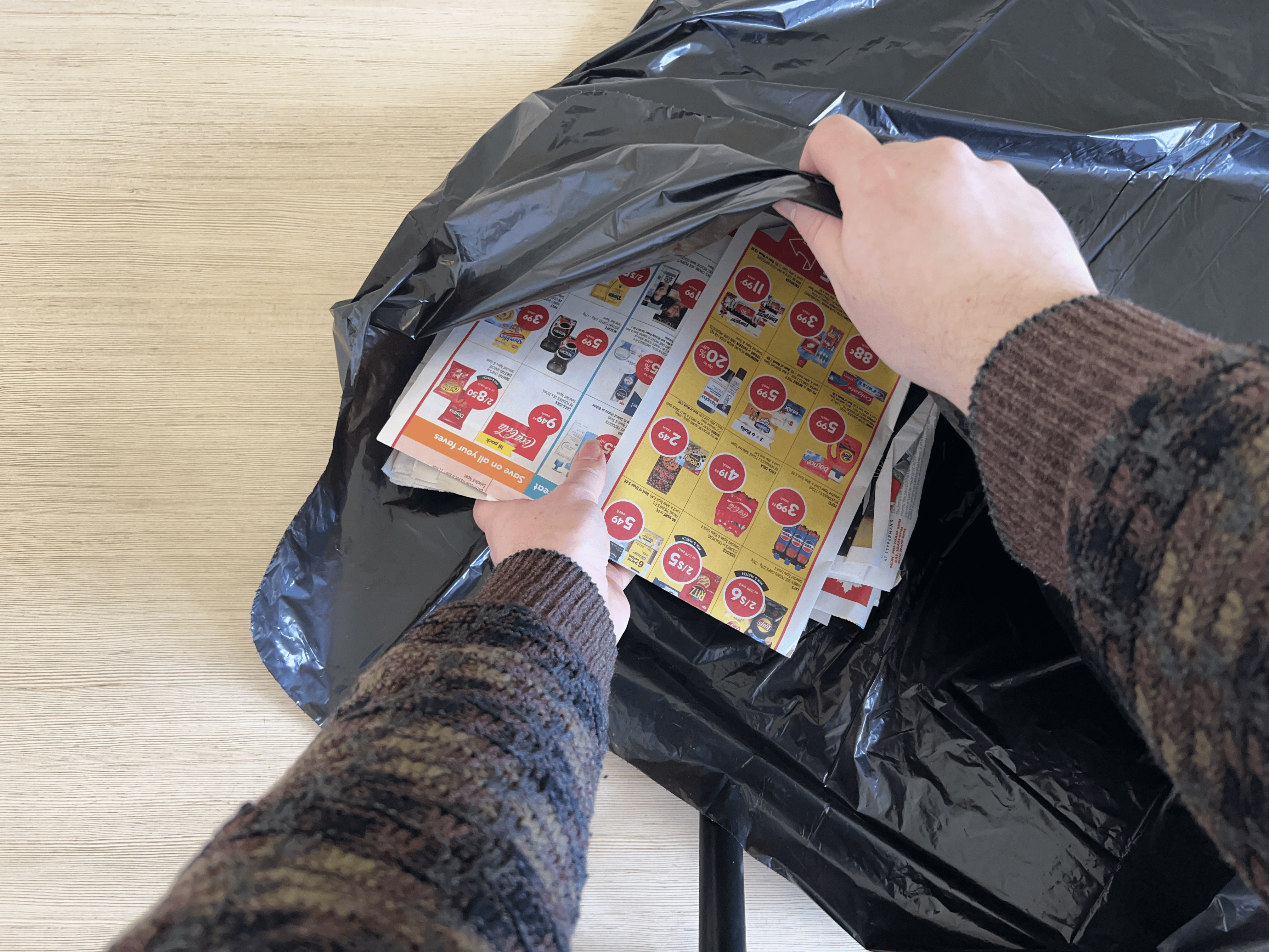 A pair of hands pushing some newspaper into a garbage bag.
