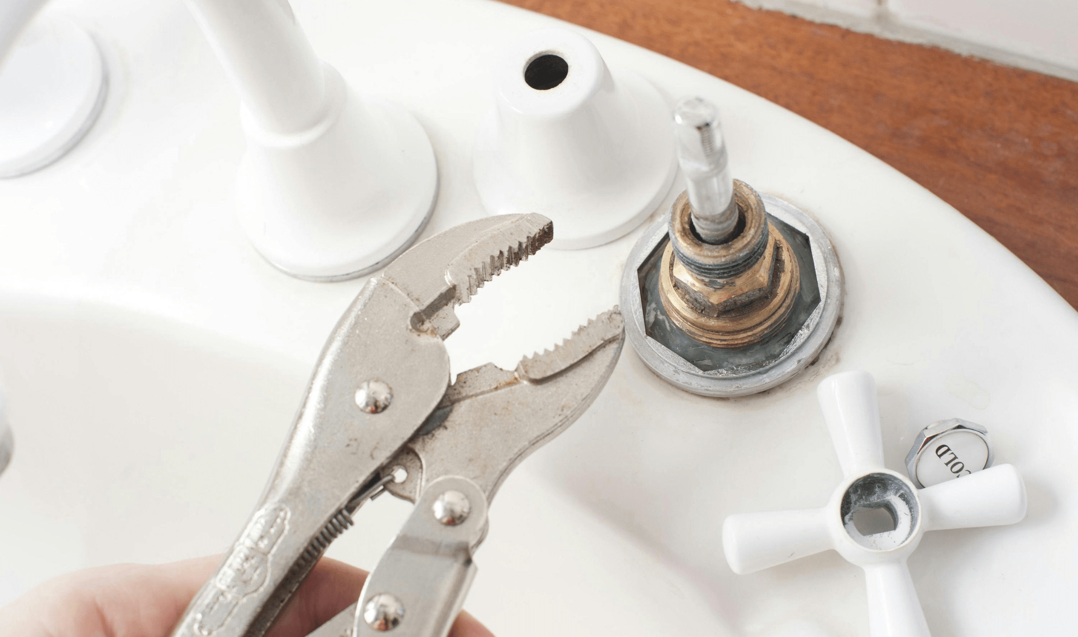 A hand using an adjustable wrench to remove a sink handle.