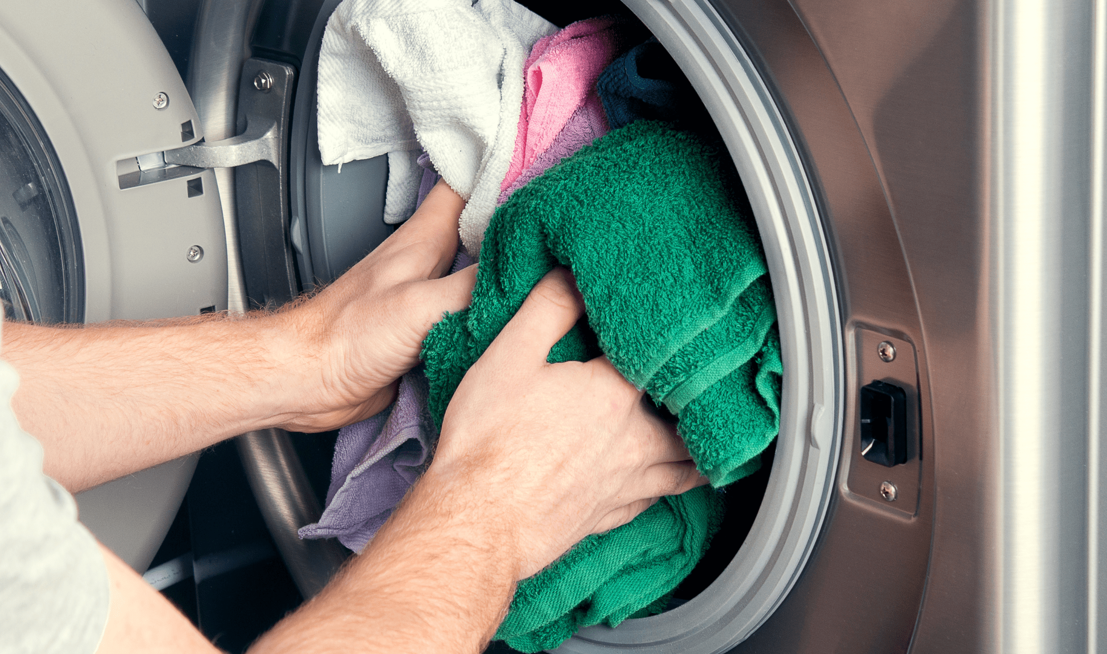 A pair of hands putting a load of laundry in a washing machine.