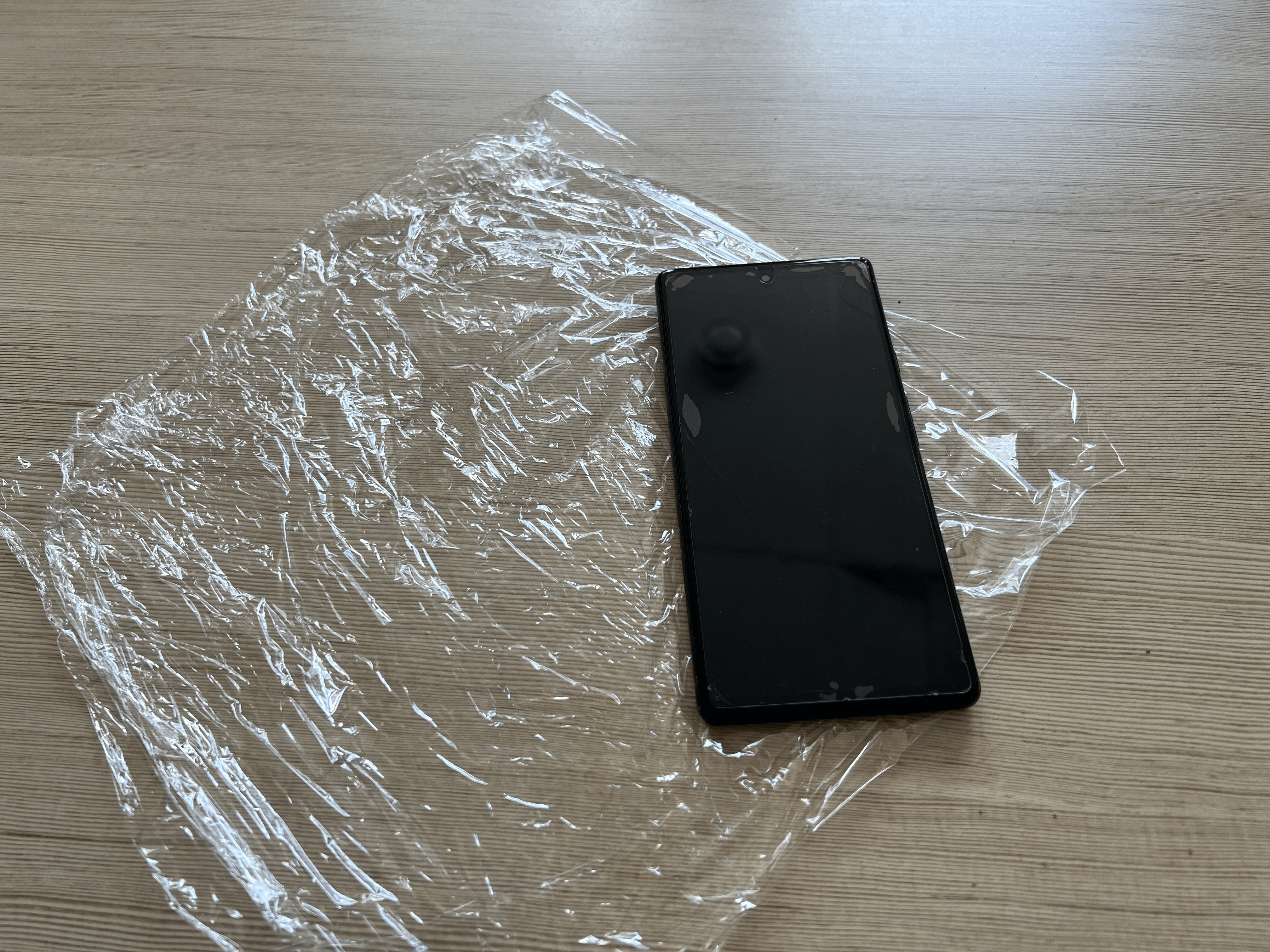 A smartphone sitting atop a piece of plastic wrap on a table.