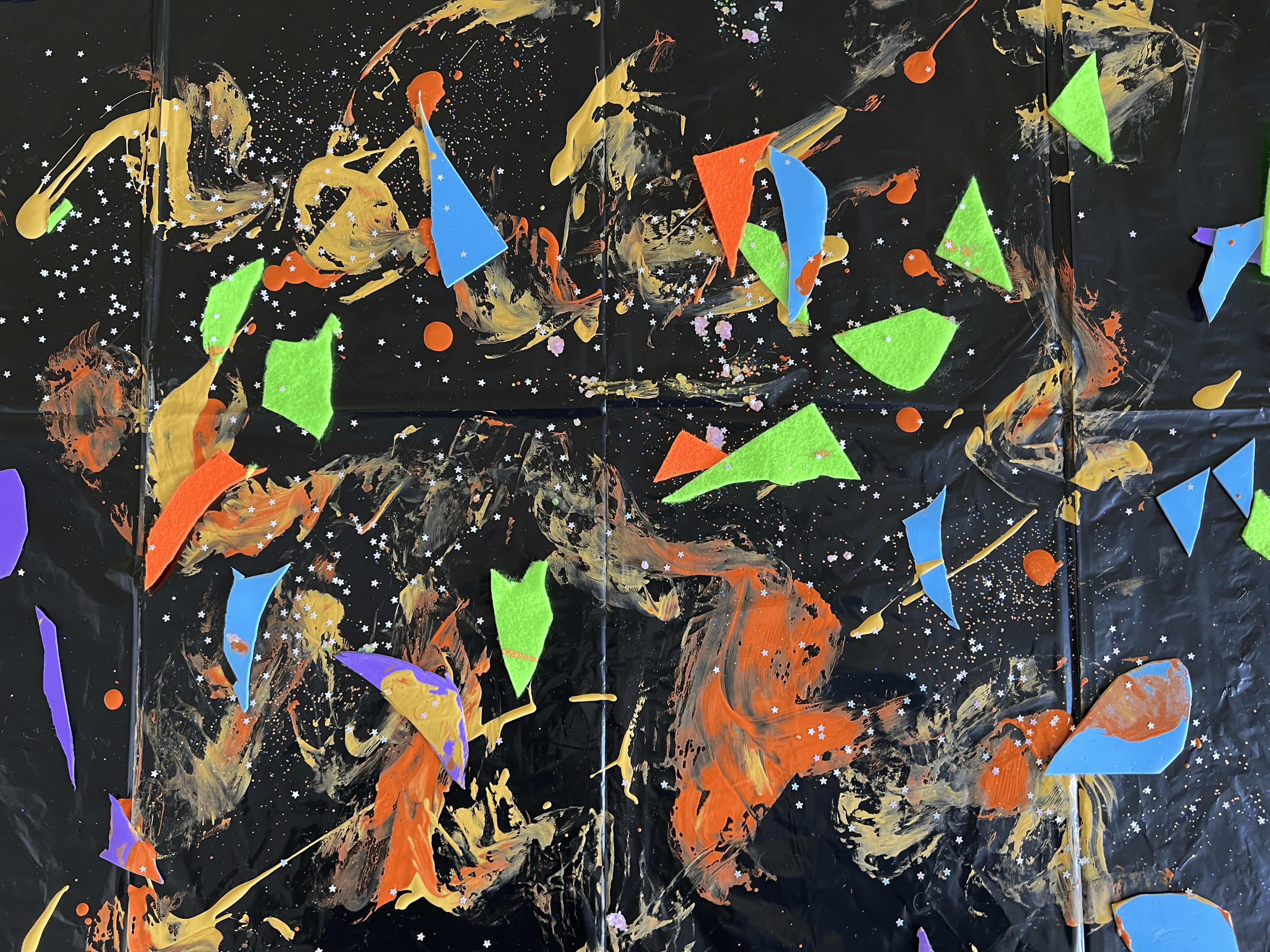 Craft mess, paint, glitter, and cut up foam/felt on a garbage bag surface.
