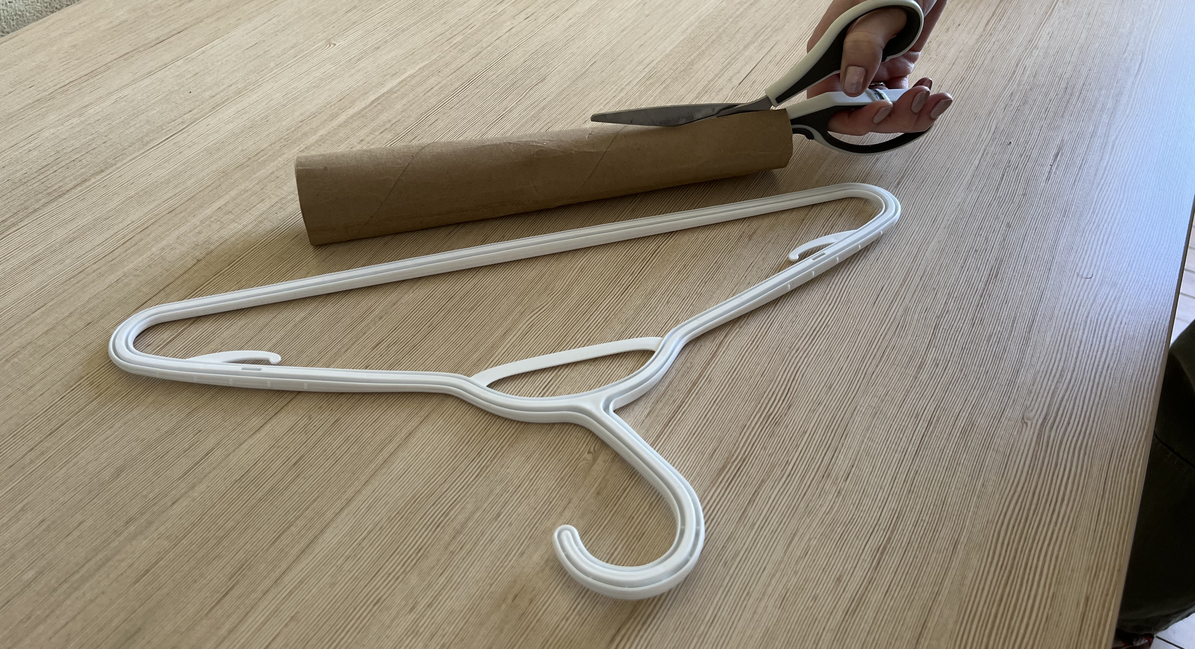 A hand cutting a cardboard tube that's next to a plastic coat hanger.