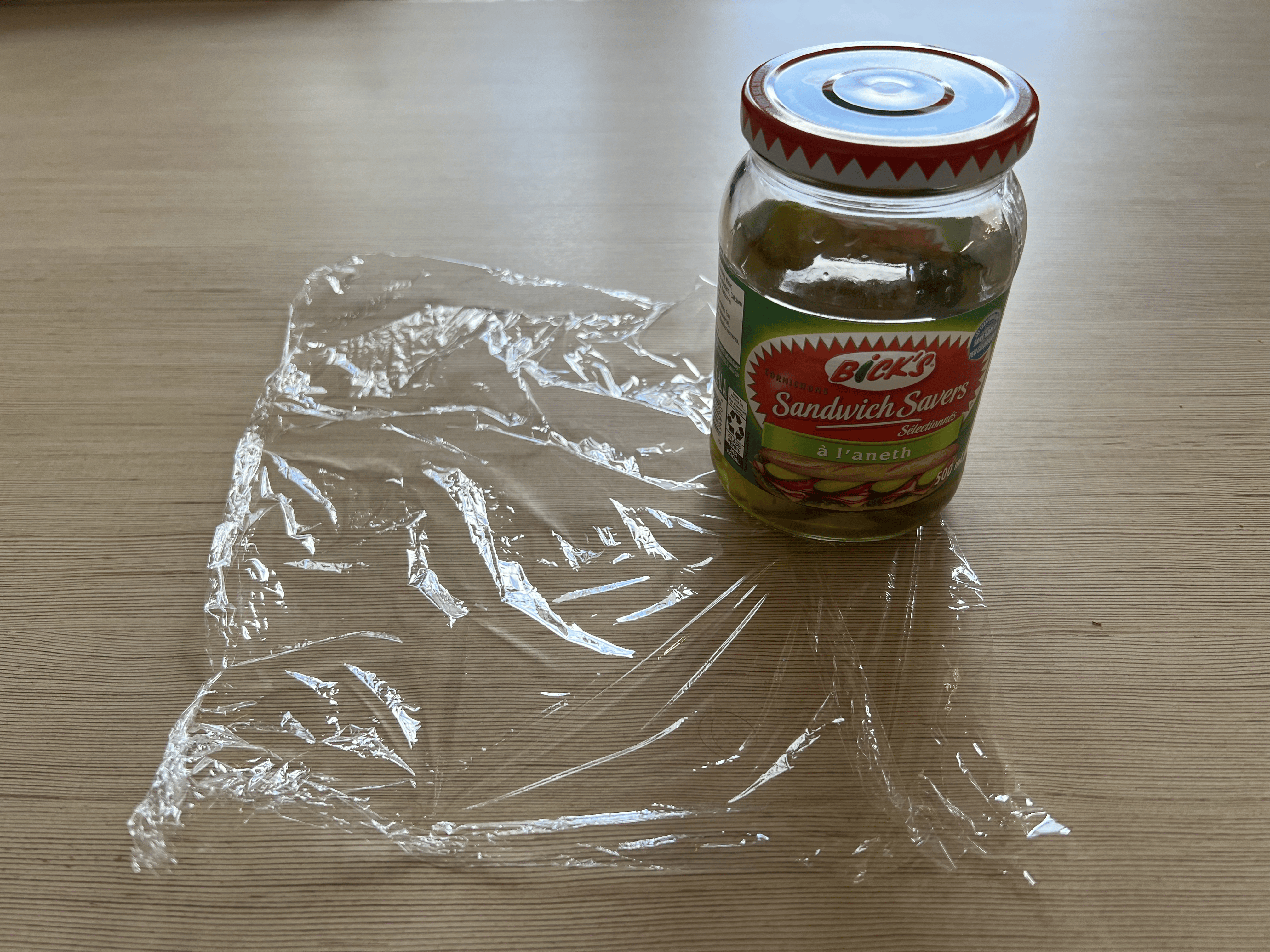 A jar of pickles on top of a piece of plastic wrap.