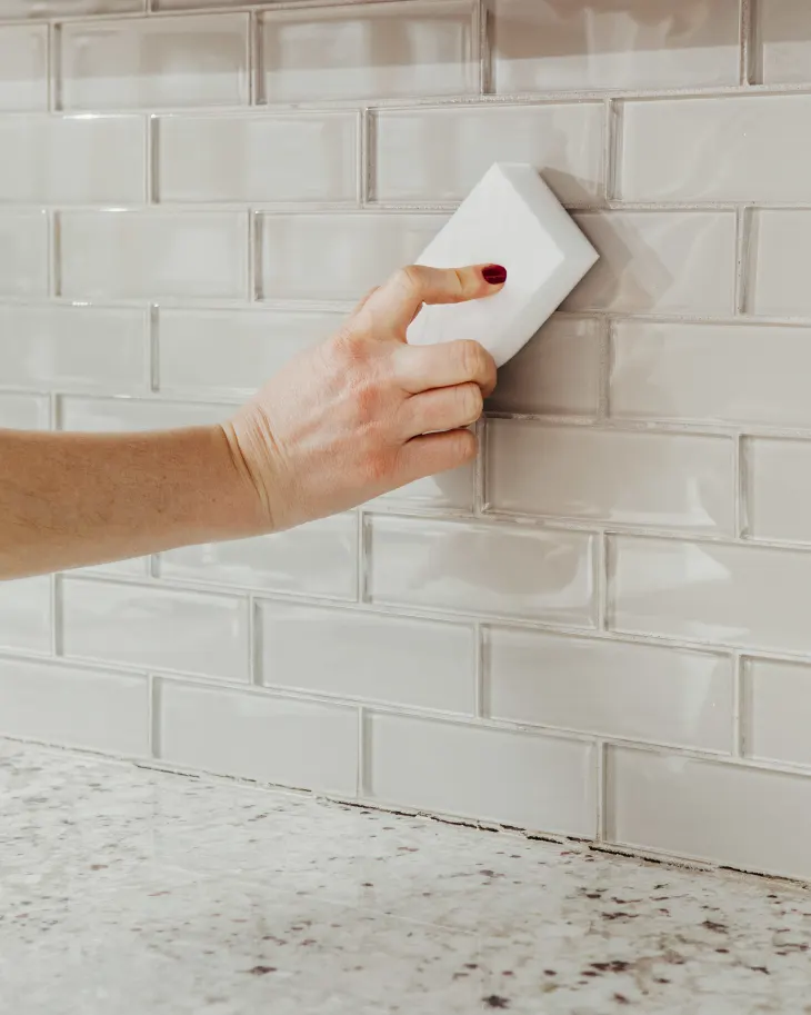 A hand wiping a kitchen backsplash with a melamine sponge.