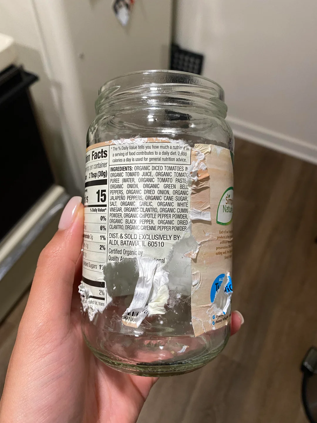 A hand holding up a jar with a half-peeled, sticky label.